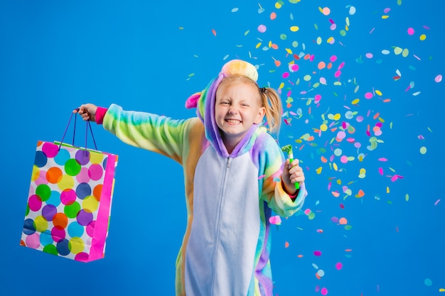 Una bambina felice in un kigurumi unicorno tiene in mano un sacchetto regalo