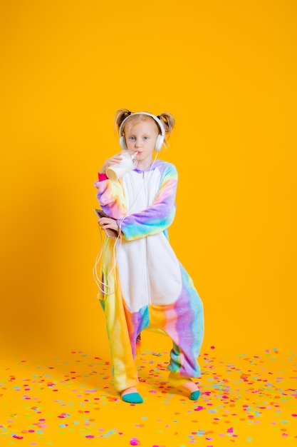 Una bambina felice in un unicorno di kigurumi ascolta musica in cuffia in possesso di uno smartphone