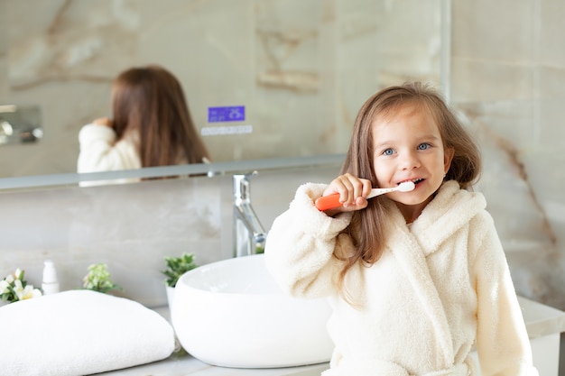 Una bambina felice in vestaglia si lava i denti davanti a uno specchio in bagno. Routine mattutina. Igiene. Foto di alta qualità