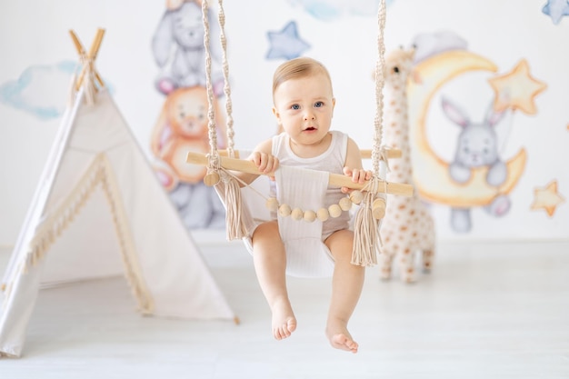 una bambina felice o un ragazzino con un corpo bianco oscilla su un altalena nella nursery il bambino si diverte sorridendo o ridendo