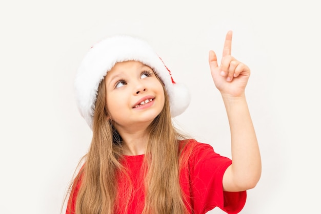 Una bambina felice punta il dito di lato su un muro bianco.