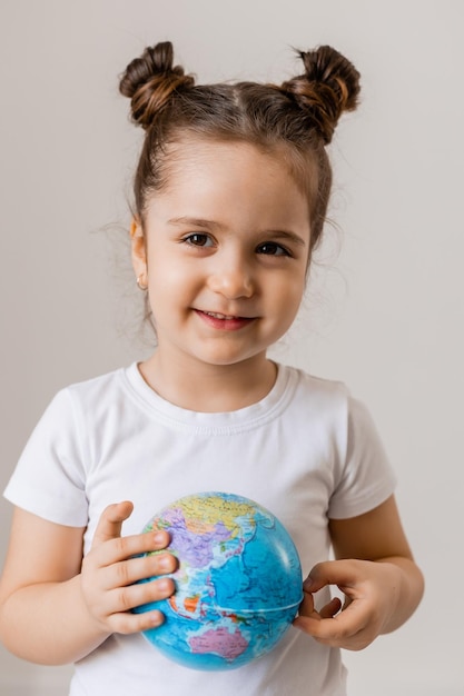 Una bambina felice tiene in mano un piccolo pianeta globo in una maglietta bianca su sfondo bianco Earth Day spazio per il testo