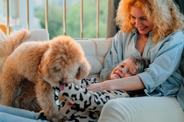 Una bambina felice, un bambino con un sorriso, gioca in una vernada primaverile estiva a casa con mamma e un cane