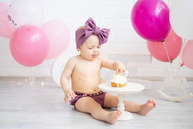 Una bambina festeggia il suo primo anno di compleanno con palloncini rosa e mangia la sua torta con le mani sorride e si rallegra