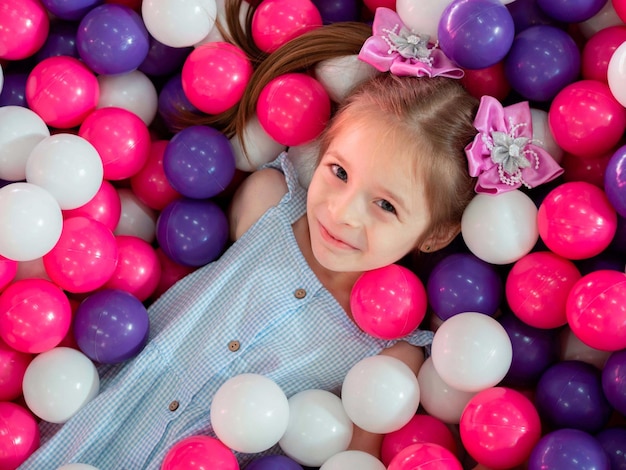 Una bambina giace sorridente in palline di plastica colorate in una grande piscina asciutta.