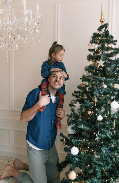 Una bambina gioca con il papà seduto sulle sue spalle mentre decora un albero di Natale