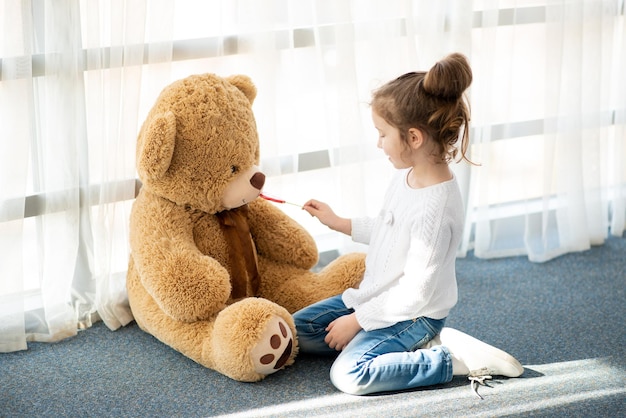 Una bambina gioca con un grande orsacchiotto È vestita con un maglione bianco Childhood Lifestile