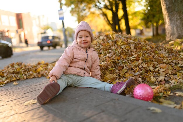 Una bambina gioca in un mucchio di foglie autunnali