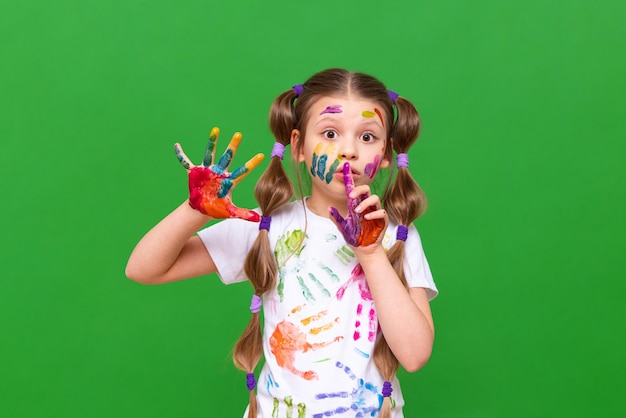 Una bambina gioiosa con le mani macchiate di vernice fa facce e sorrisi una bambina si è sporcata in un rack su uno sfondo verde isolato