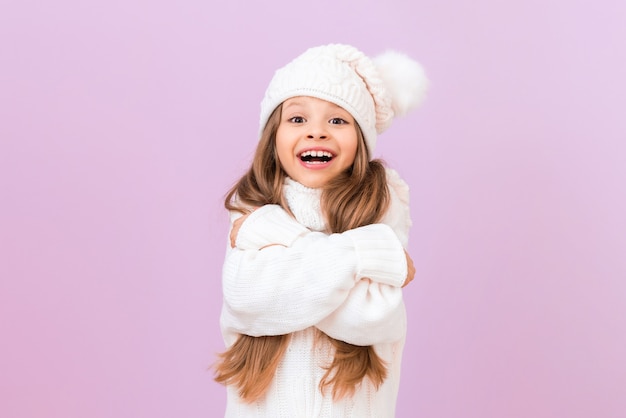 Una bambina gioiosa con un caldo cappello invernale tiene le mani vicino al petto.