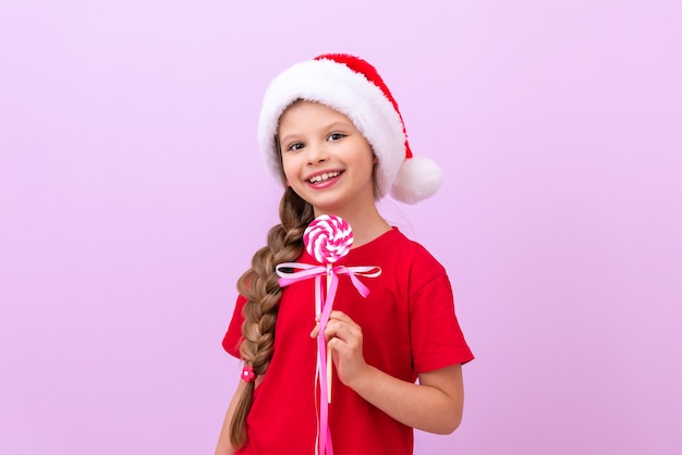 Una bambina gioiosa con un cappello di Capodanno tiene in mano un grande lecca-lecca.