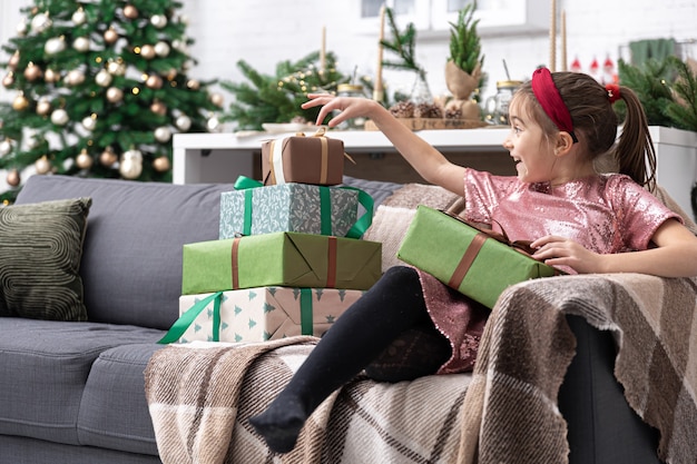 Una bambina gode di molti regali di Natale seduta sul divano di casa