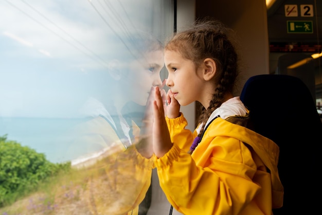 Una bambina guarda fuori dal finestrino di un treno al mare Viaggio Riflessione Estate Vacanza in famiglia