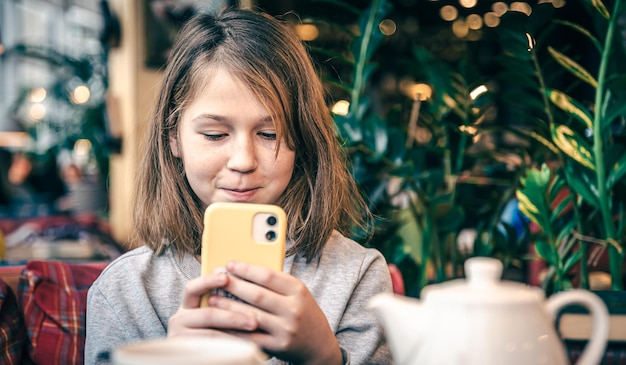 Una bambina guarda lo schermo dello smartphone mentre è seduta in un bar