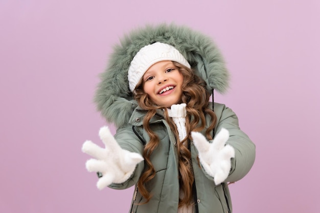 Una bambina in abiti invernali e capelli ricci tira le mani in avanti e sorride al bambino con una calda giacca invernale e un cappello bianco su uno sfondo viola isolato