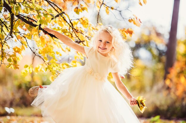 Una bambina in abito bianco che sorride su uno sfondo di foglie gialle