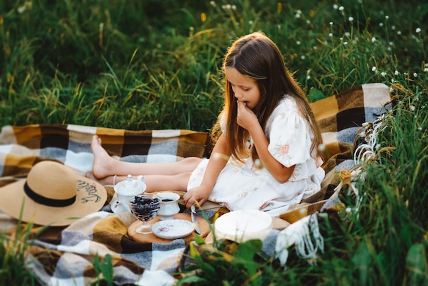 Una bambina in abito bianco mangia i mirtilli in giardino durante un picnic