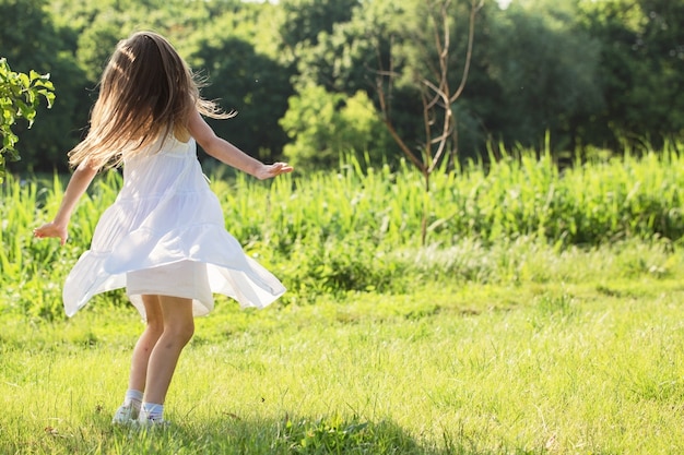 Una bambina in abito bianco sta ballando sull'erba al fiume