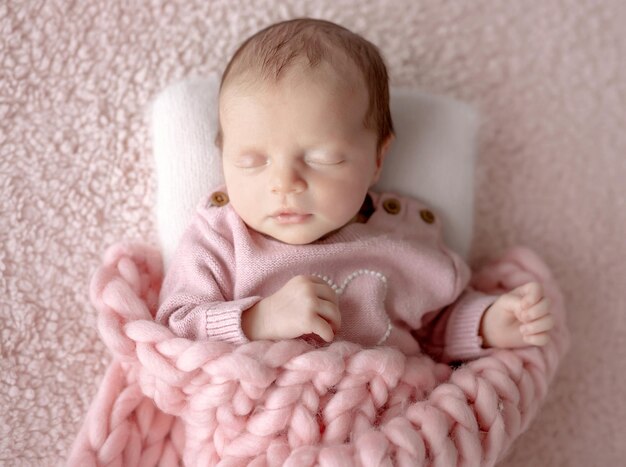 Una bambina in abito rosa dorme durante una sessione fotografica di neonati in studio