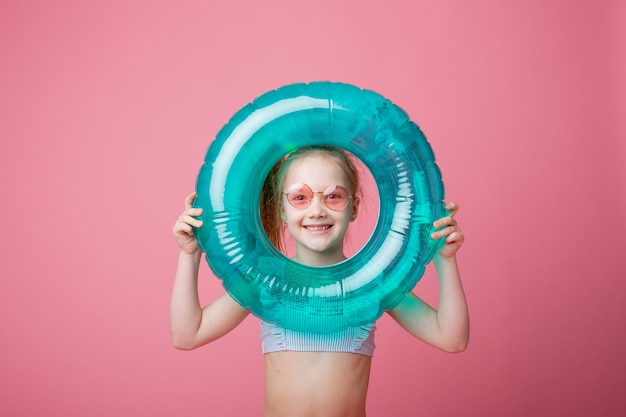 Una bambina in costume da bagno con un cerchio di nuoto su sfondo rosa