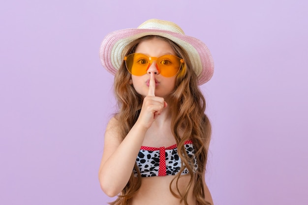 Una bambina in costume da bagno mostra un gesto del dito per favore taci.