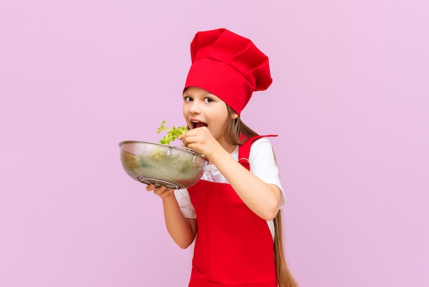 Una bambina in costume da chef Tiene in mano un'insalata e si presenta con un nuovo piatto di verdure fresche