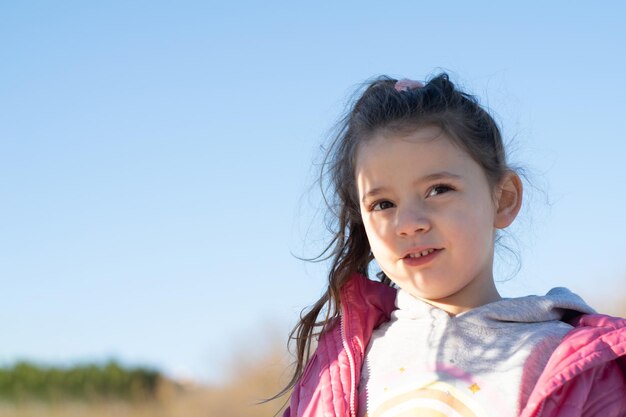 una bambina in età prescolare con una giacca rosa sorride sullo sfondo di un cielo blu il sole la illumina