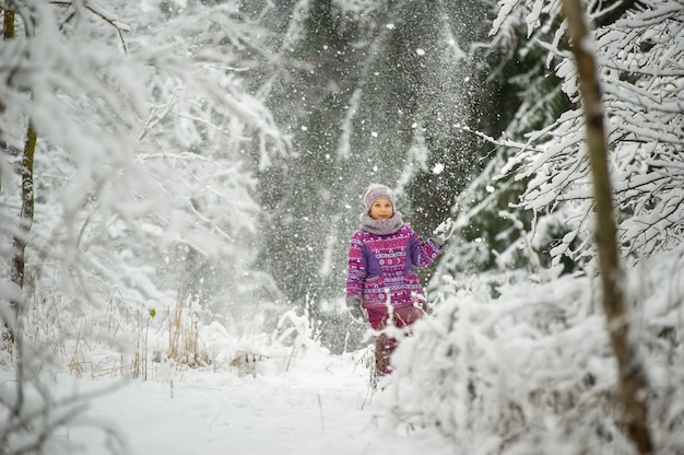 Una bambina in inverno in abiti viola cammina attraverso una foresta innevata