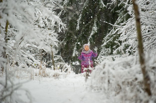 Una bambina in inverno in abiti viola cammina attraverso una foresta innevata