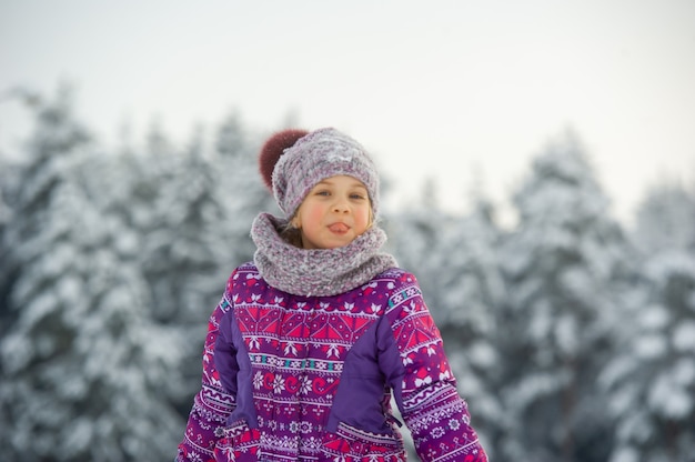 Una bambina in inverno in abiti viola cammina attraverso una foresta innevata