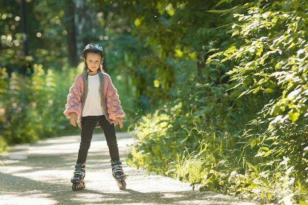 Una bambina in maglione rosa con cerniera pattina nel parco sui suoi rulli