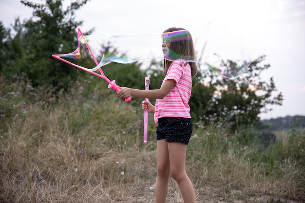 Una bambina in natura gioca con grandi bolle di sapone.