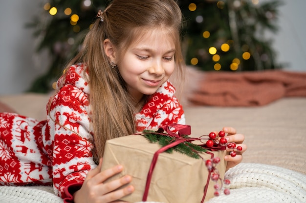 Una bambina in pigiama la mattina presto ha trovato un regalo di Babbo Natale sotto l'albero