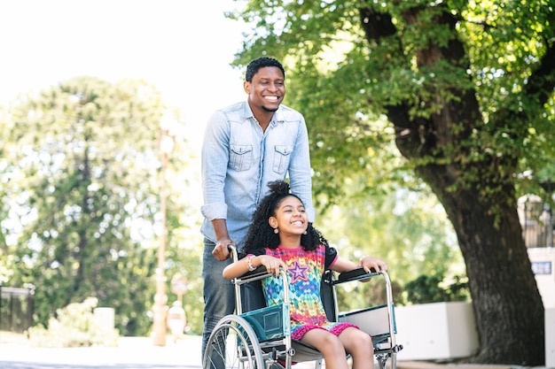 Una bambina in sedia a rotelle che si diverte e si diverte con suo padre durante una passeggiata insieme all'aperto