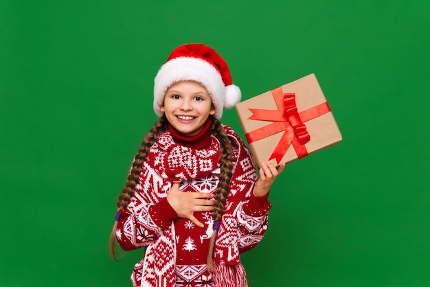 Una bambina in un caldo maglione di Natale tiene un regalo e sorride il concetto del nuovo anno isolato sullo sfondo