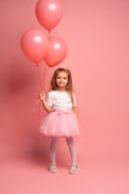 Una bambina in un tutù rosa con in mano tre palloncini rossi