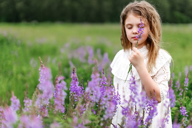 Una bambina in un vestito bianco con bellissimi fiori nel campo d'estate