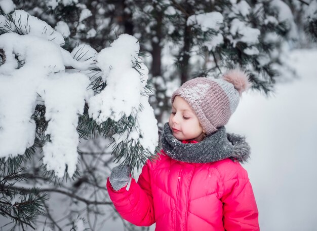 Una bambina in una giacca luminosa gioca nella foresta innevata d'inverno.