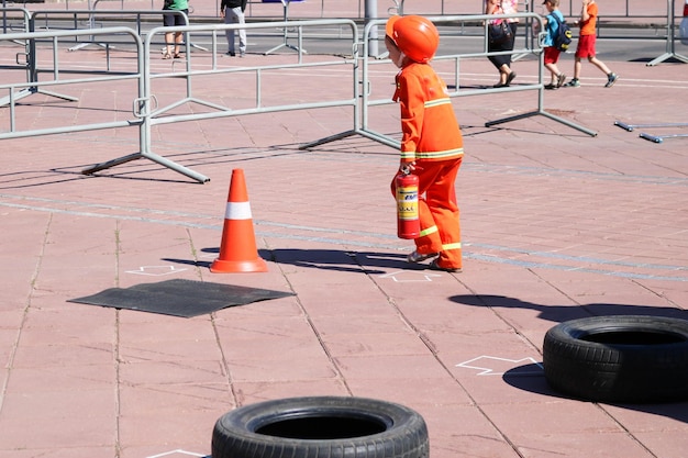 Una bambina in una tuta ignifuga scontrosa corre con un estintore per spegnere un incendio