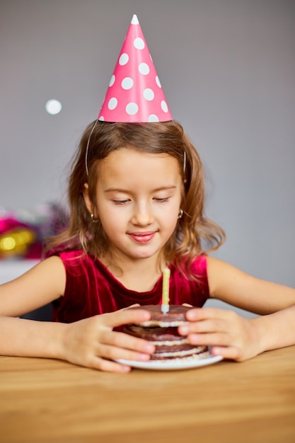 Una bambina indossa un cappello di compleanno guardando una torta di compleanno per un concetto di festa.