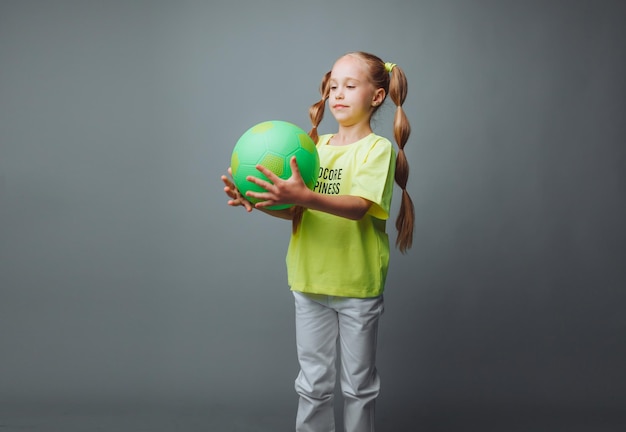 Una bambina lancia una palla isolata su uno sfondo grigio un po' di sport per bambini dell'atleta