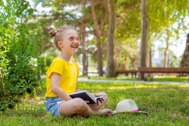 Una bambina legge un libro sull'erba nel parco in estate