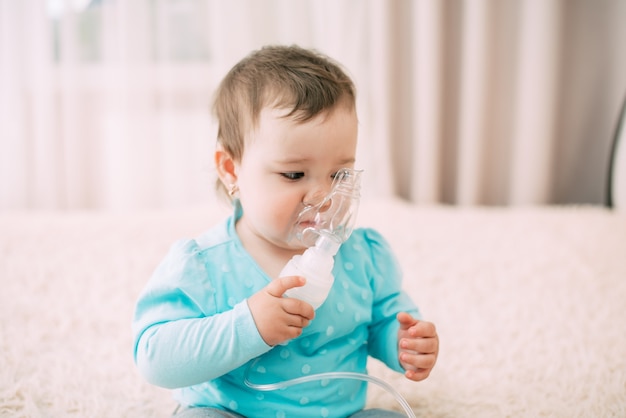 Una bambina lei stessa che tiene la maschera del nebulizzatore, facendo l'inalazione