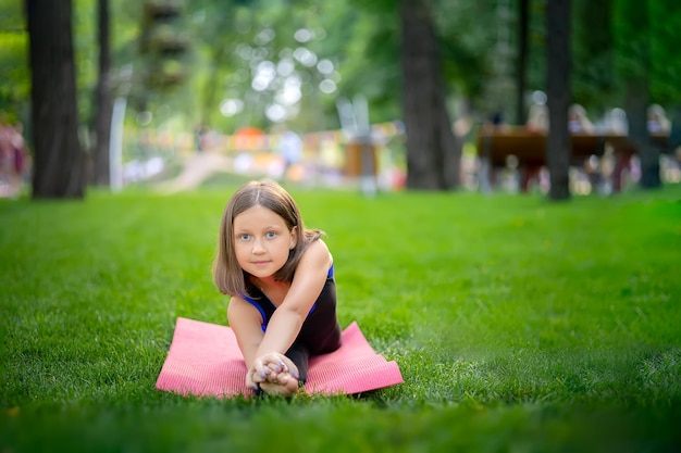Una bambina nel parco sta facendo yoga stretching appoggiandosi sulla gamba Una ragazza è seduta su uno spago