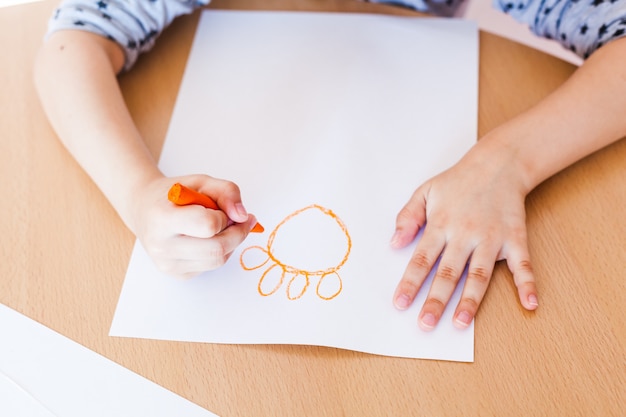 Una bambina piccola e carina si siede a un tavolo e disegna