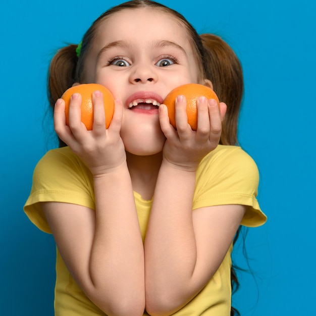 Una bambina piccola e sorridente tiene in mano due mandarini su sfondo blu