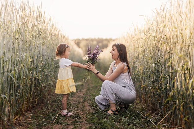 Una bambina regala un mazzo di lupini a sua madre sul campo d'estate. Concetto di amore e famiglia felice