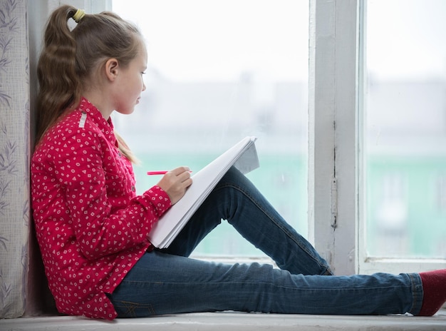 Una bambina seduta su un davanzale e guardando nella finestra