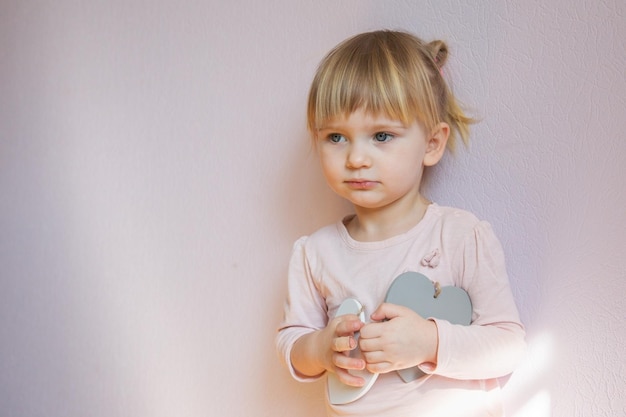 Una bambina seria Una bambina con i capelli biondi tiene in mano due cuori bianchi di legno
