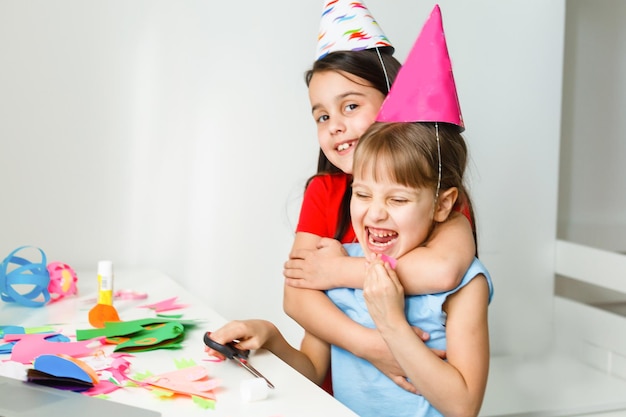 Una bambina, si curva e ride davanti a un laptop con un berretto. Festeggia il compleanno via internet in tempo di quarantena, autoisolamento e valori familiari, compleanno online. Congratulazioni all'animatore